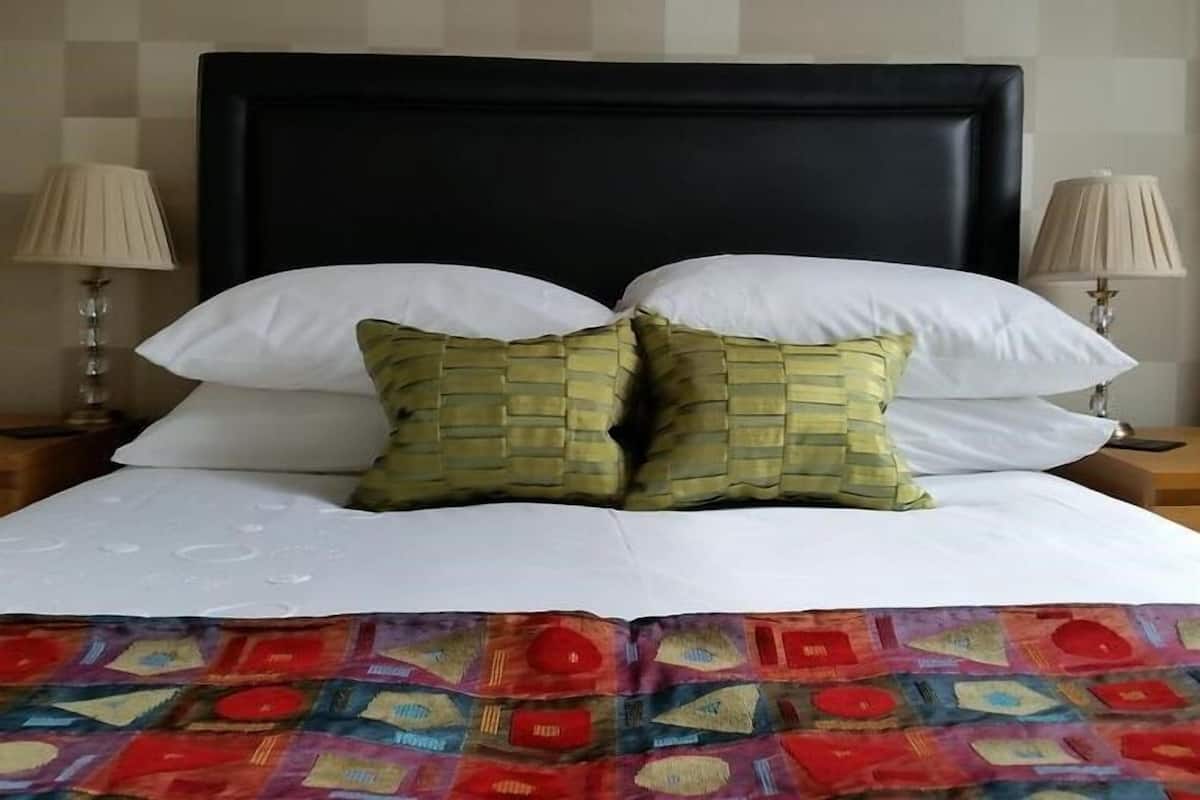A bed with white linens, two white pillows, and two green pillows with a woven pattern. There are two bedside lamps with beige shades.