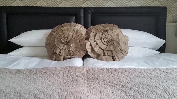 Una cama con una colcha blanca con textura y dos almohadones beige grandes y con flecos.