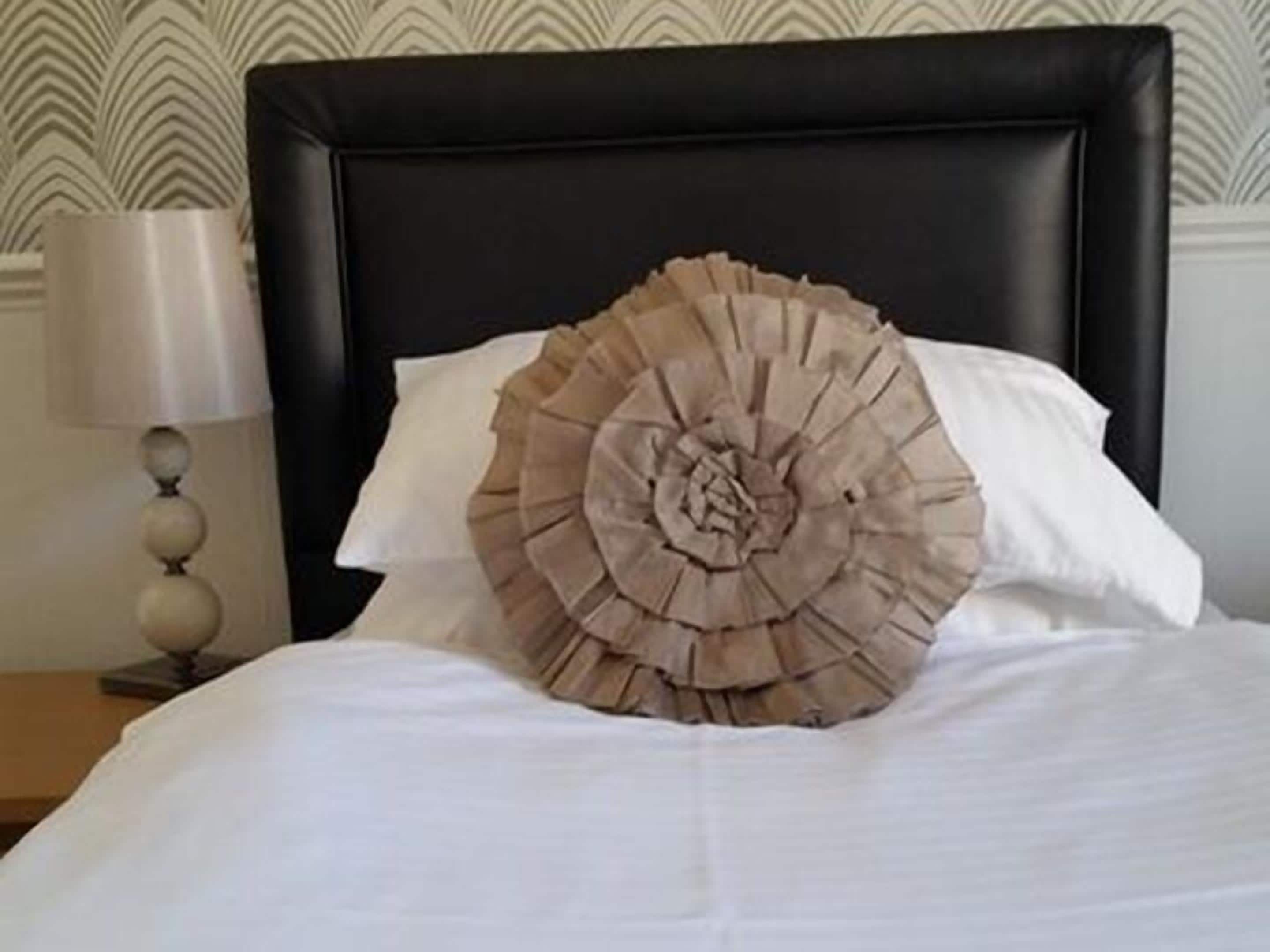 Una cama con un cojín decorativo con flecos y una lámpara de noche.