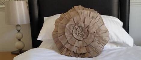 Una cama con un cojín decorativo con flecos y una lámpara de noche.
