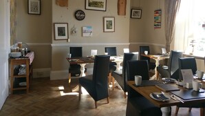 Un comedor con mesas y sillas de madera, obras de arte enmarcadas en las paredes y una araña.