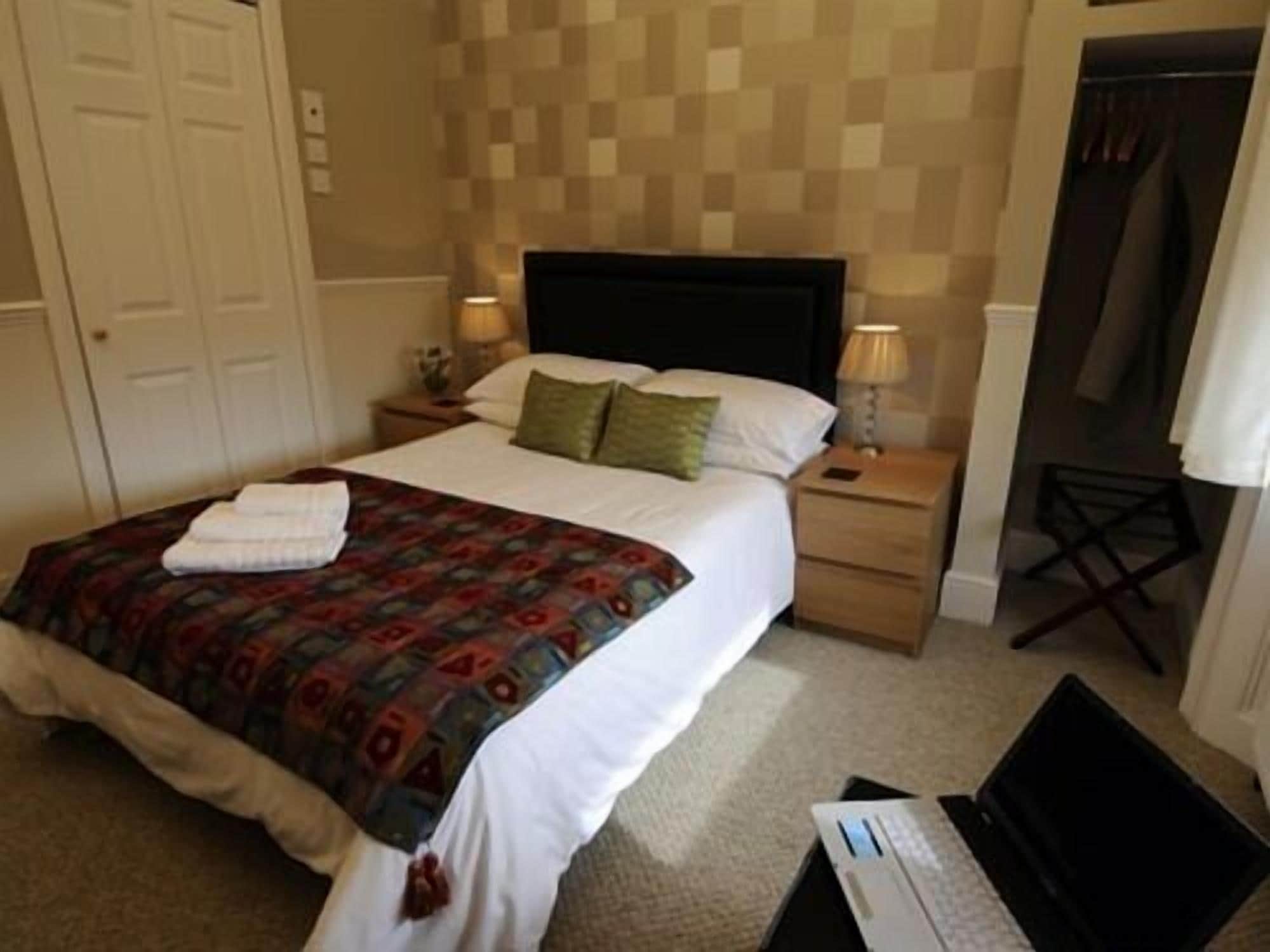 A hotel room with a bed, two bedside tables, a lamp, a laptop, and a coat rack.