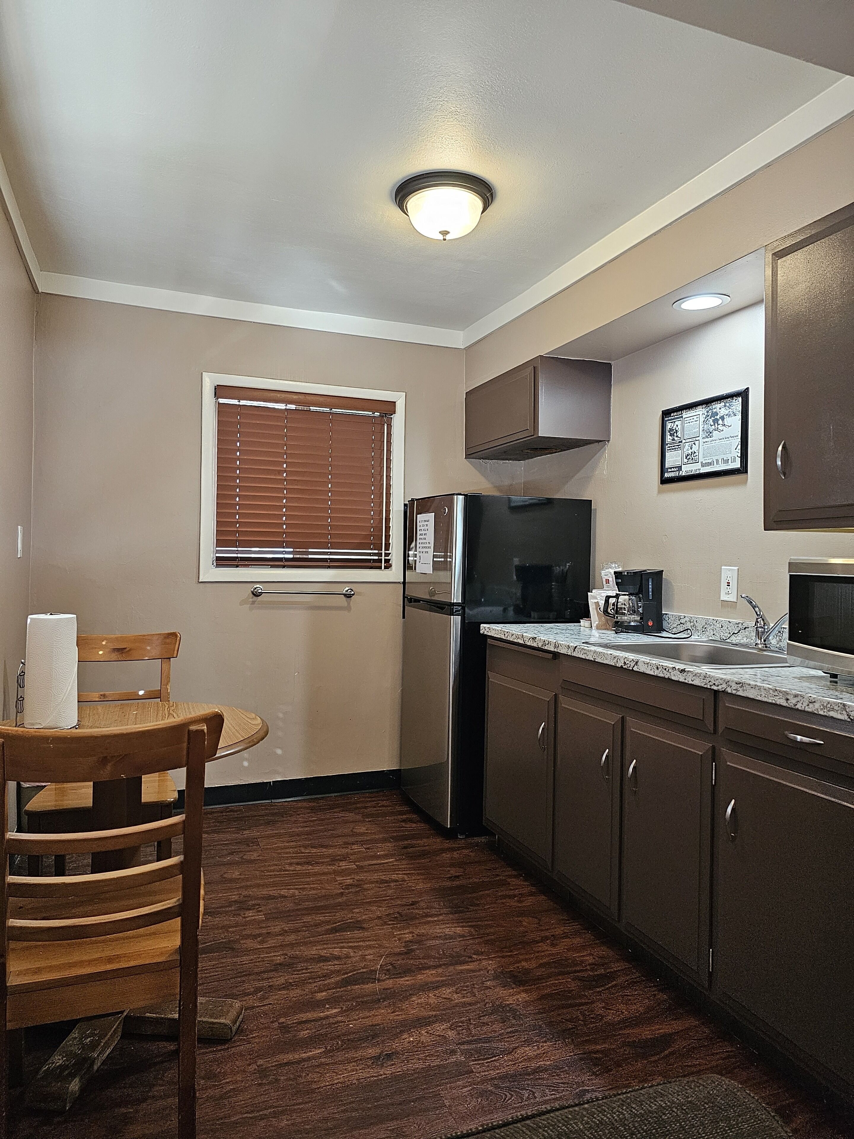 A compact kitchen with a refrigerator, stove, microwave, and a small dining area with a chair and table.