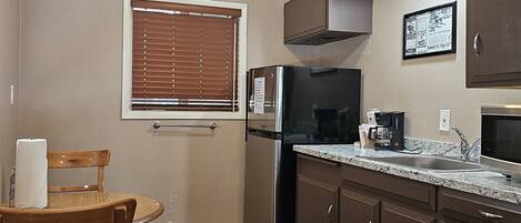 A compact kitchen with a refrigerator, stove, microwave, and a small dining area with a chair and table.
