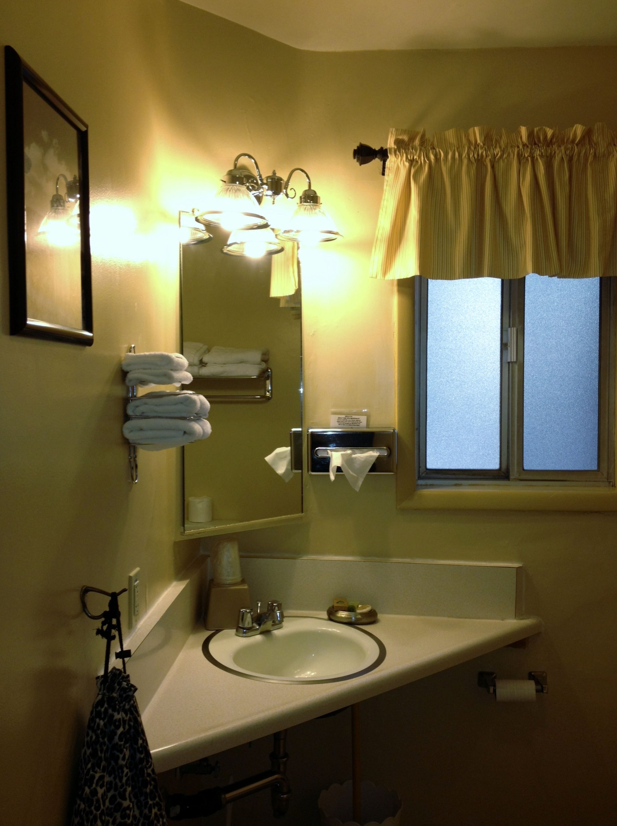 Casa de banho com lavatório, espelho, porta-toalhas e janela com cortinas.