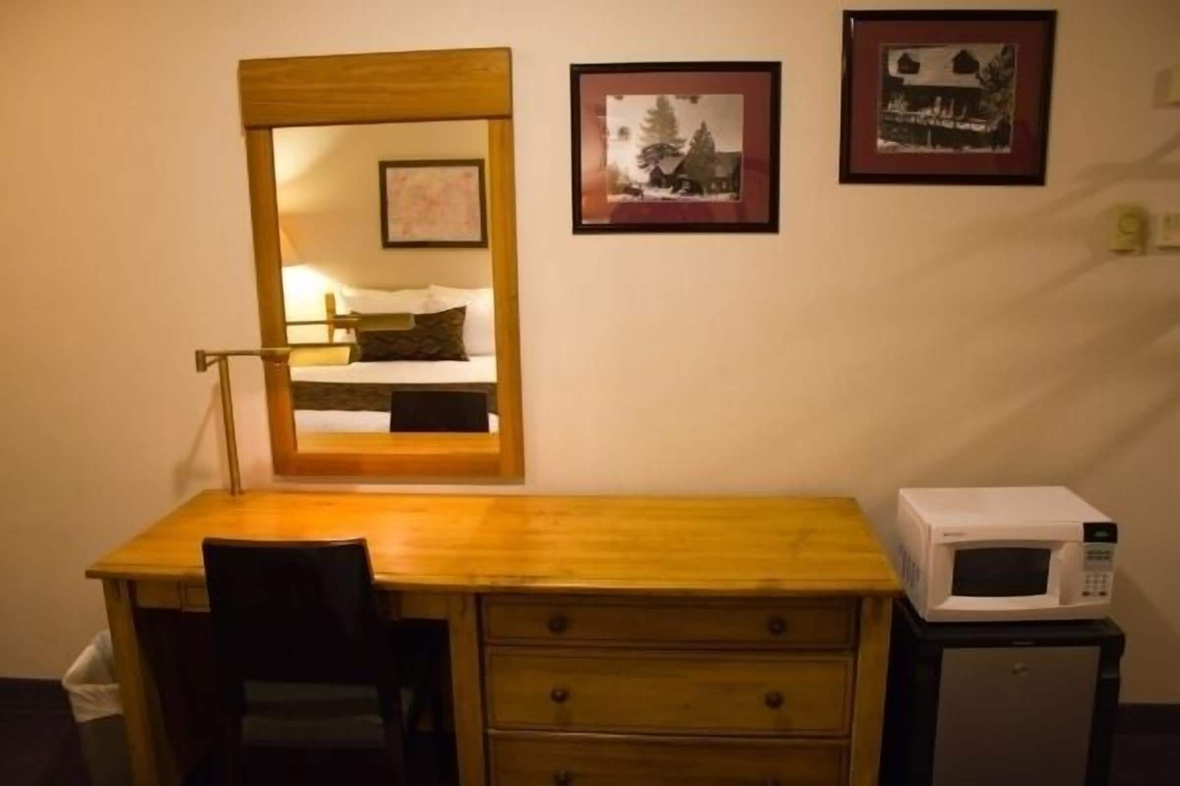 Una habitación pequeña con un escritorio de madera, una silla, un espejo, un microondas y dos cuadros en la pared.