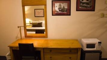 Una habitación pequeña con un escritorio de madera, una silla, un espejo, un microondas y dos cuadros en la pared.