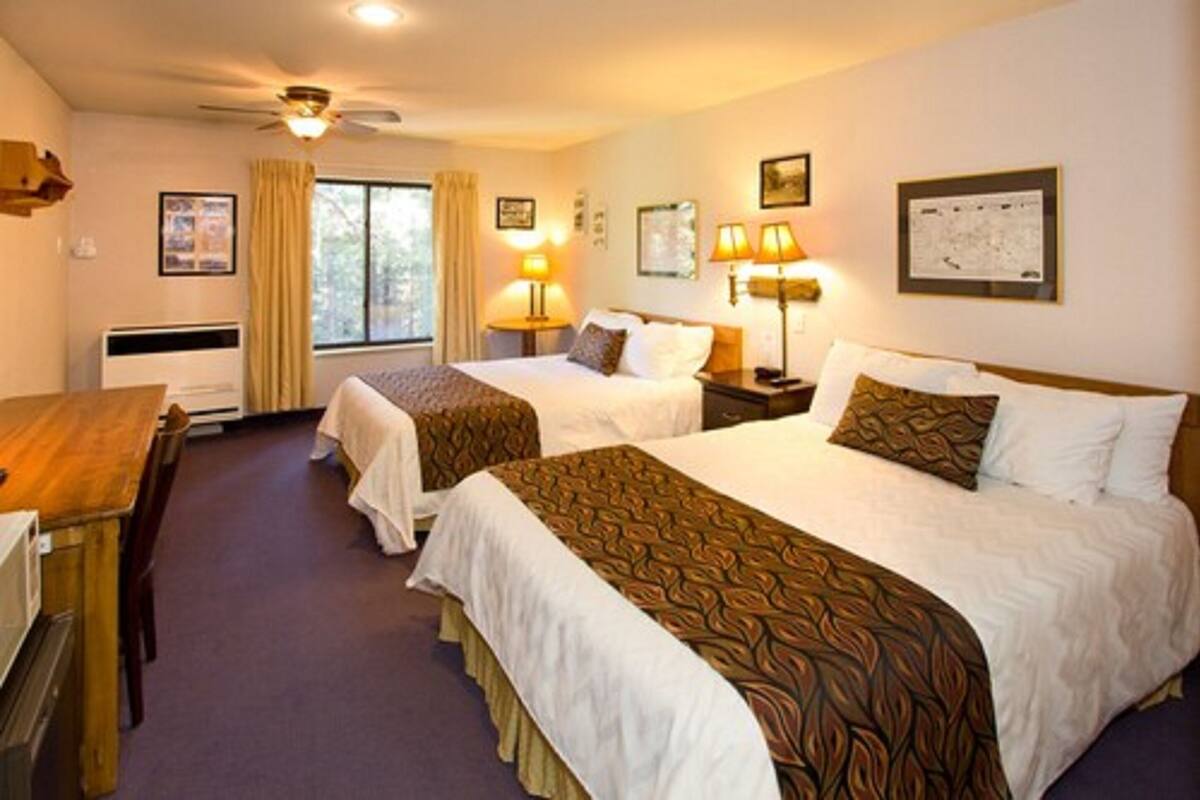 A hotel room with two beds, a desk, and a window.