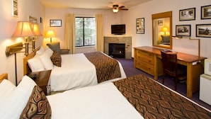 A hotel room with two beds, a desk, a television, a fireplace, and framed pictures on the wall. - Holiday Haus Motel (Mammoth Lakes)