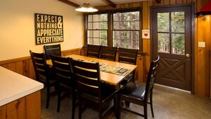 A dining room with a wooden table and chairs, a wall-mounted sign, and a door with a window view. - Holiday Haus Motel (Mammoth Lakes)
