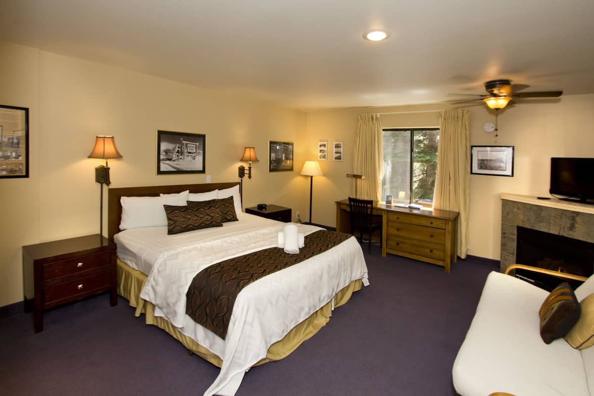 A hotel room with a large bed, a desk, a television, and a fireplace.