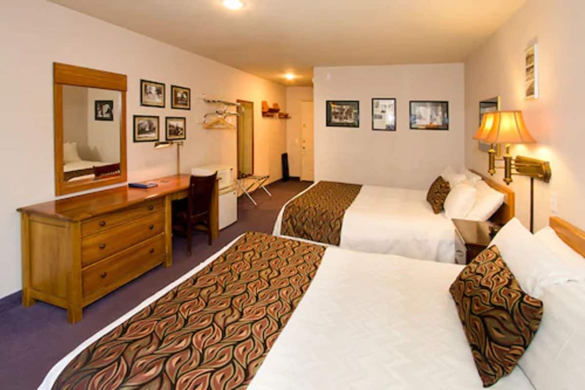 A hotel room with two single beds, a wooden dresser, a desk, a chair, and a mirror.