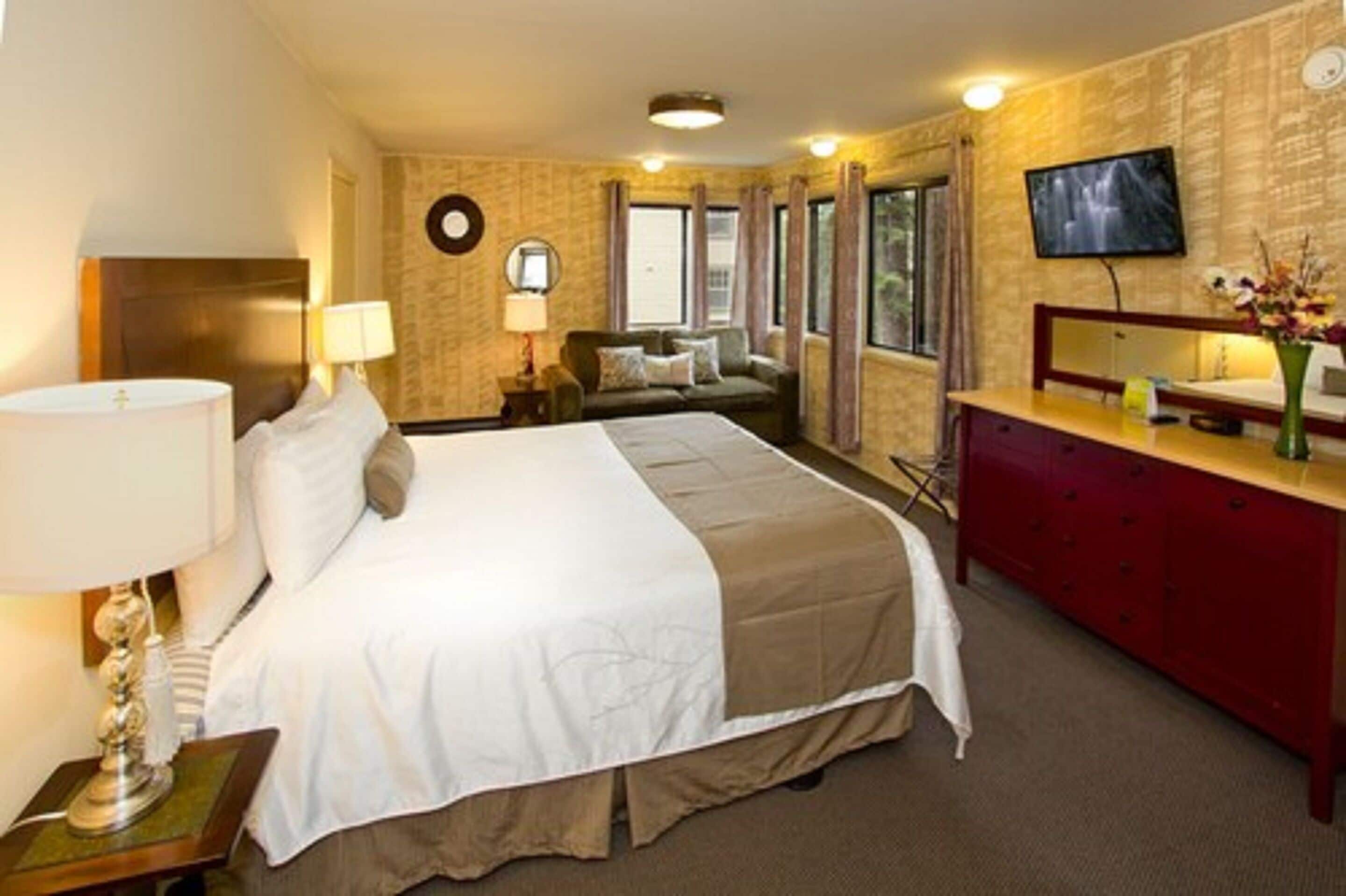 Ett hotellrum med en stor säng, ett skrivbord med en spegel, en TV och ett fönster med gardiner.
