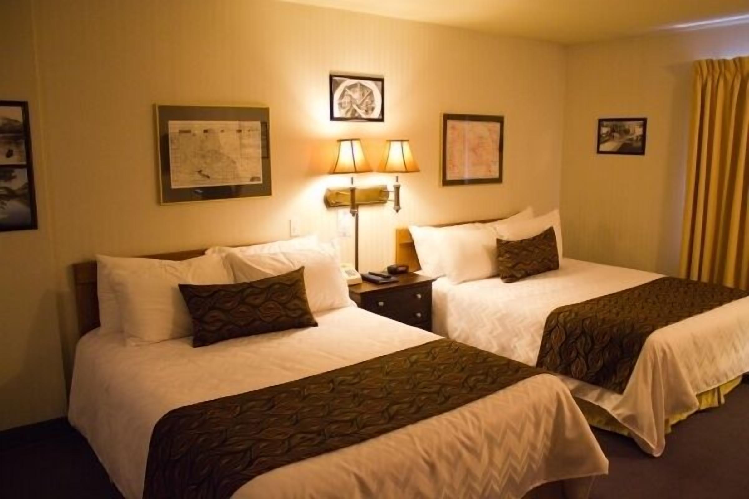 Una habitación de hotel con dos camas, una mesita de noche con lámparas y cuadros en las paredes.