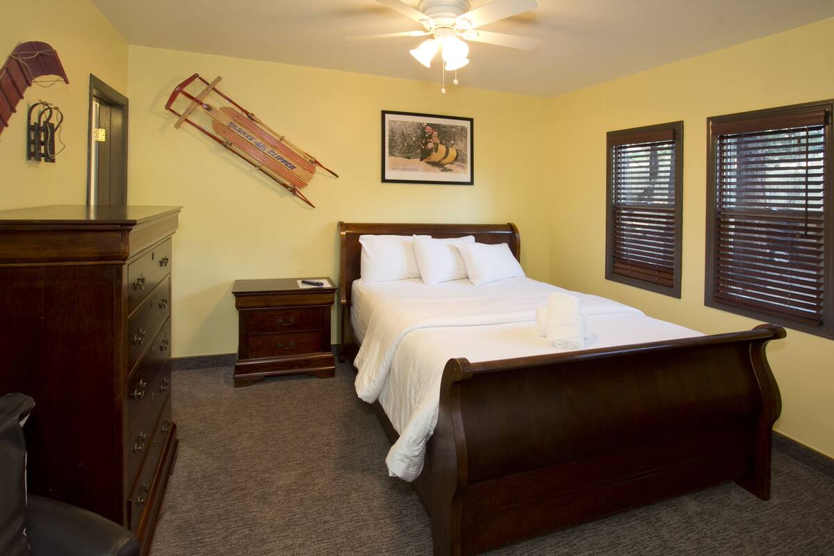 A bedroom with a wooden bed, a nightstand, a dresser, a ceiling fan, and a framed picture on the wall.