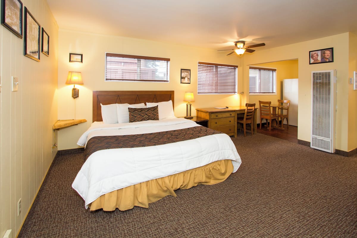 A hotel room with a large bed, two bedside lamps, a desk with a chair, and a ceiling fan.