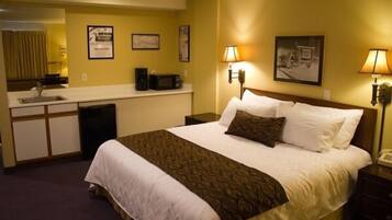A hotel room with a bed, bedside lamps, a microwave, a sink, and a framed picture on the wall.