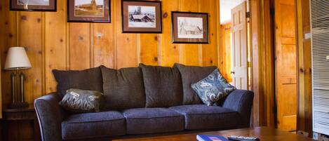 A wooden-paneled room with a sofa, a table, and framed pictures on the wall.