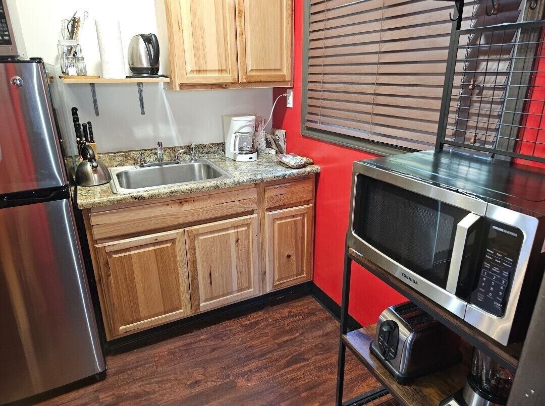 A compact kitchen with wooden cabinets, a stainless steel refrigerator, a microwave, and a coffee maker.