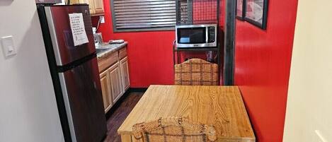 A compact kitchen with a refrigerator, microwave, and wooden table.