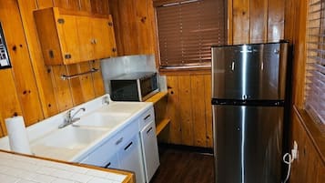 Cocina compacta con paredes de madera, un refrigerador de acero inoxidable, un microondas y un lavamanos con encimera blanca.