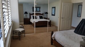 A bedroom with a large mirror, a bed, a nightstand, a chair, and two lamps. - Beaconlea Tower Apartments (Labrador)