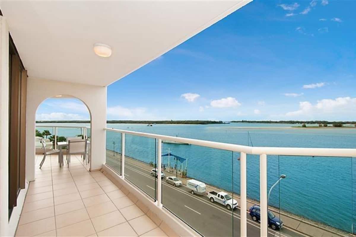 A balcony with a view of a body of water and a road with vehicles.