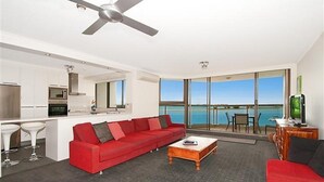 A modern living room with a red sofa, a coffee table, and a view of the sea through large windows. - Beaconlea Tower Apartments (Labrador)