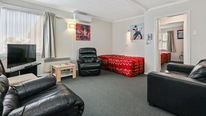 A modern living room with a flat-screen TV, leather sofas, a red patterned sofa, a wooden coffee table, and artwork on the walls. - Arcadia Motel (Christchurch)