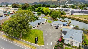 A motel with a parking lot, a small lake, and mountains in the background. - Arcadia Motel (Christchurch)