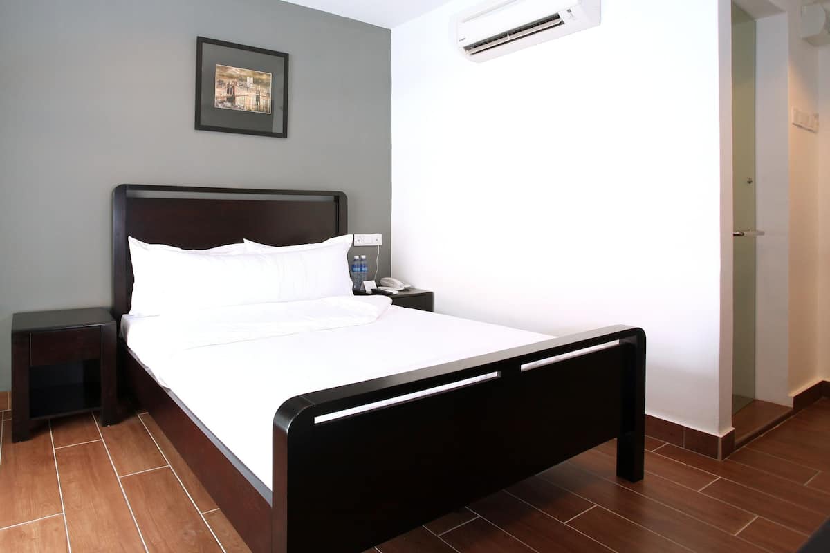 Habitación de hotel con cama, mesita de noche, aire acondicionado y un cuadro en la pared.