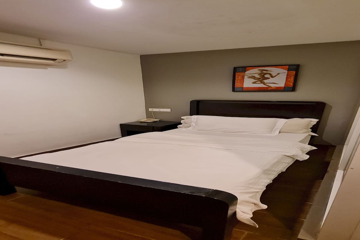 Un dormitorio con cama, mesita de noche, aire acondicionado instalado en la pared y un cuadro enmarcado.