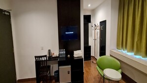 A compact hotel room with a small desk, a green chair, a mini-fridge, and a TV mounted on the wall. - Hotel O Crossroads Hotel (Kuala Lumpur)