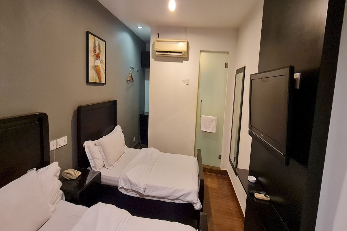 Habitación de hotel con dos camas, televisión, equipo de aire acondicionado y puerta de baño.