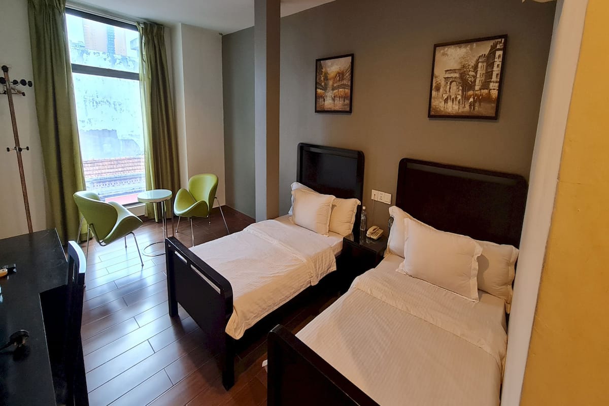 Habitación de hotel con dos camas, un escritorio, una silla, una mesita y una ventana con cortinas.