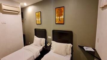A hotel room with two single beds, an air conditioner, a nightstand with a phone, and two framed pictures on the wall.