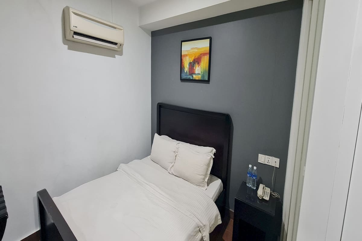 Habitación de hotel con una cama, una mesita de noche, un teléfono y un equipo de aire acondicionado.