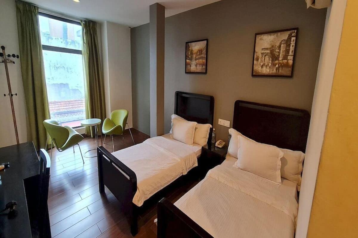 Una habitación de hotel con dos camas, un escritorio, una silla y un ventanal con cortinas.