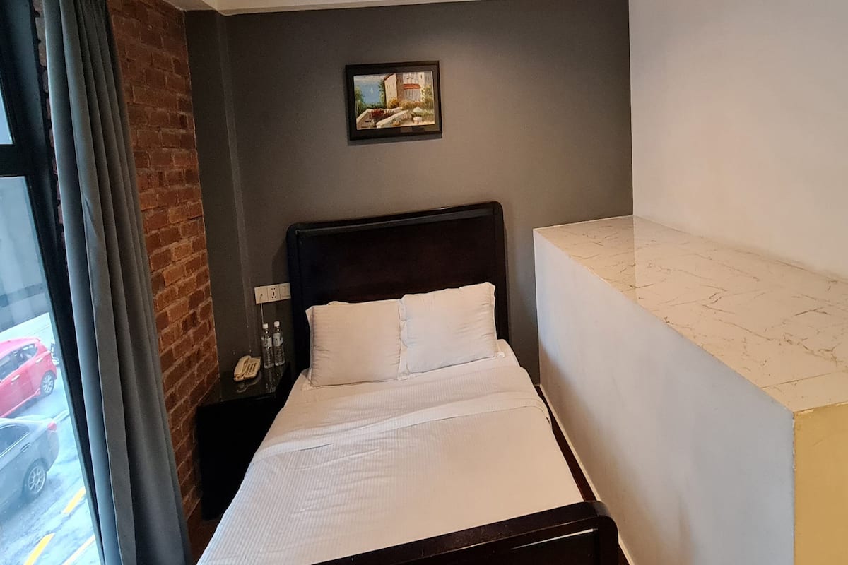 Habitación de hotel con cama, mesita de noche, un cuadro en la pared y vista a la calle.