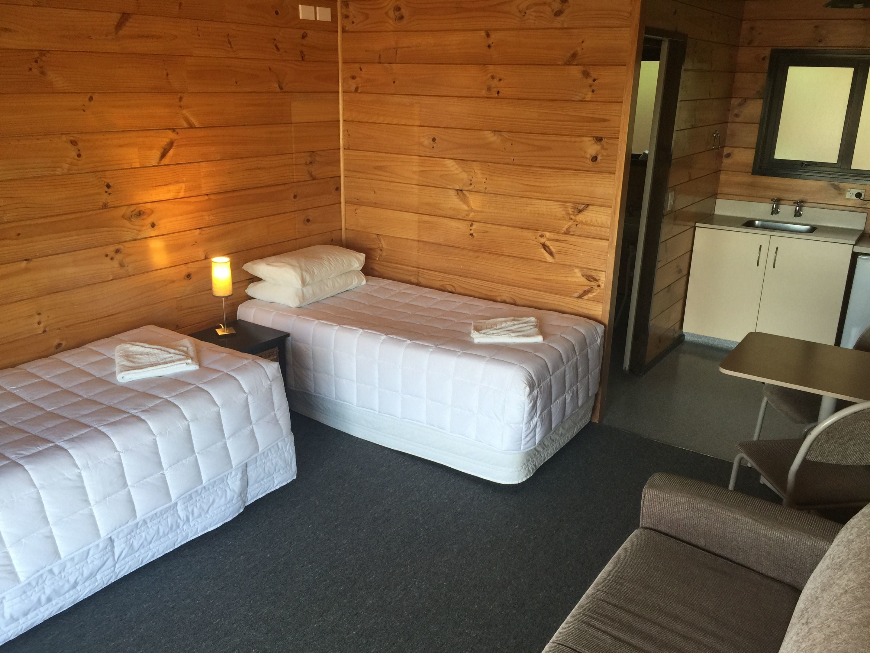 A small, cozy room with two beds, a desk, and a kitchenette.