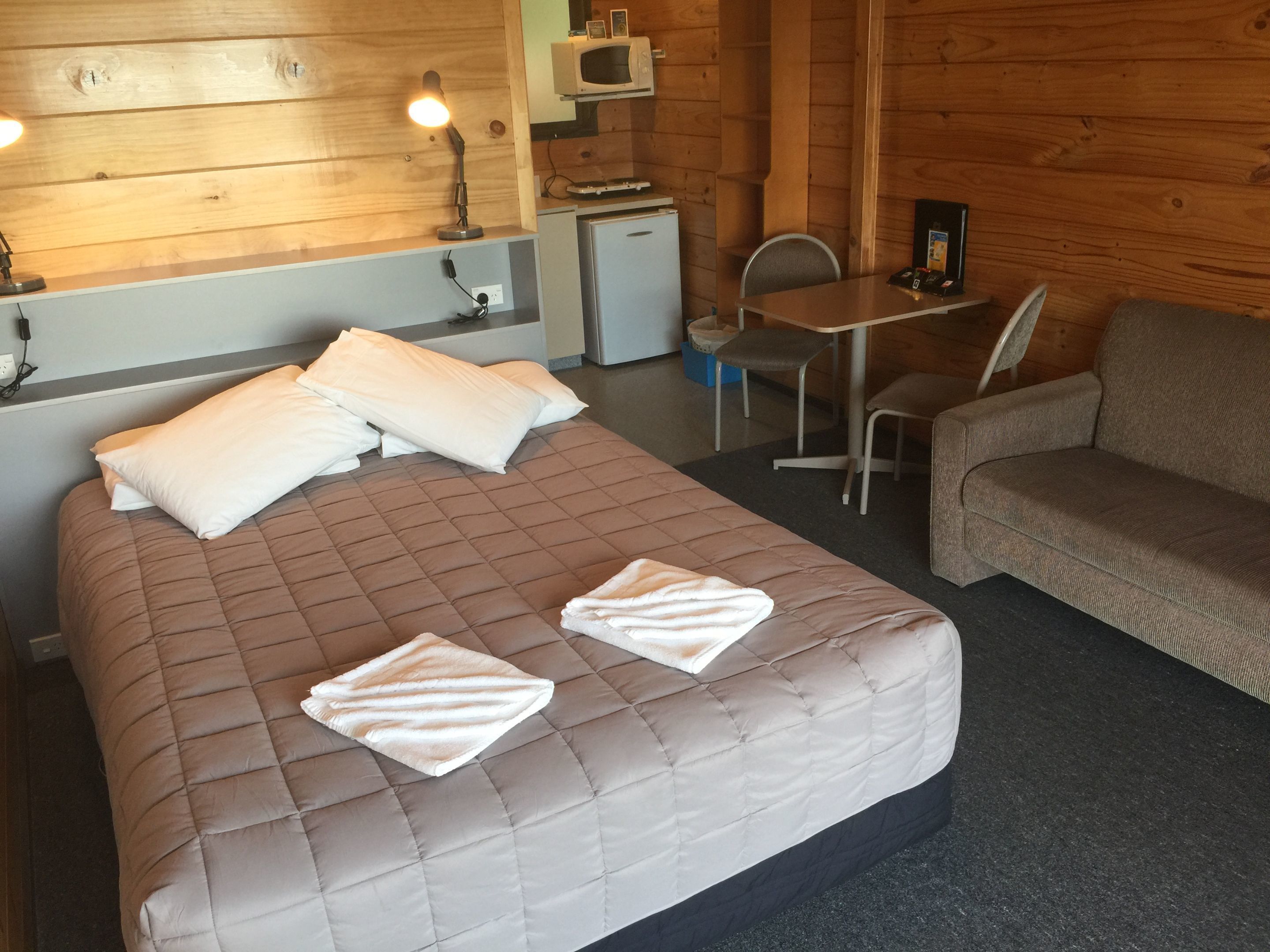 A room with a bed, a small desk, a chair, a sofa, and a microwave.