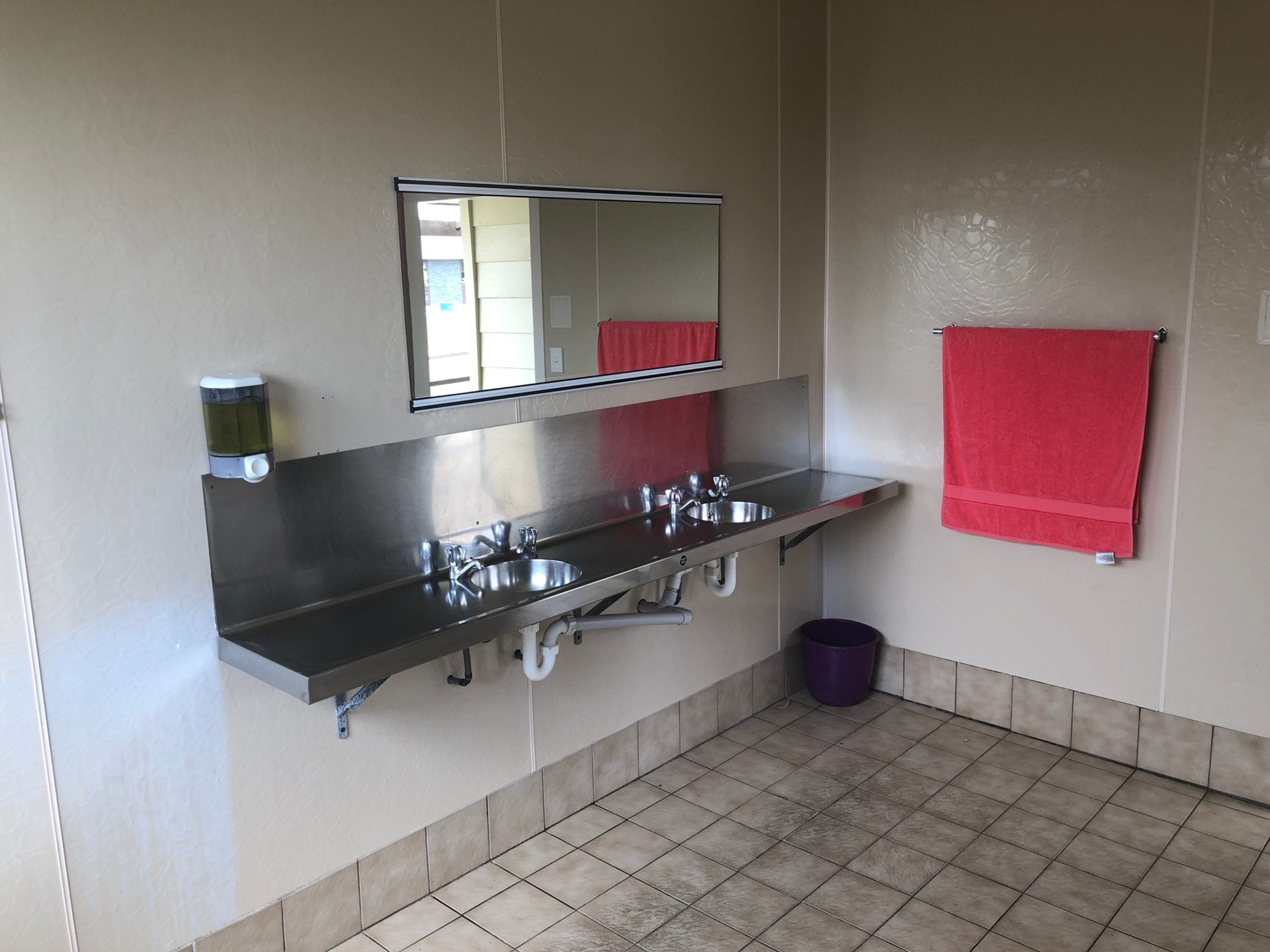 A bathroom with a stainless steel sink, a mirror, and a red towel hanging on the wall.
