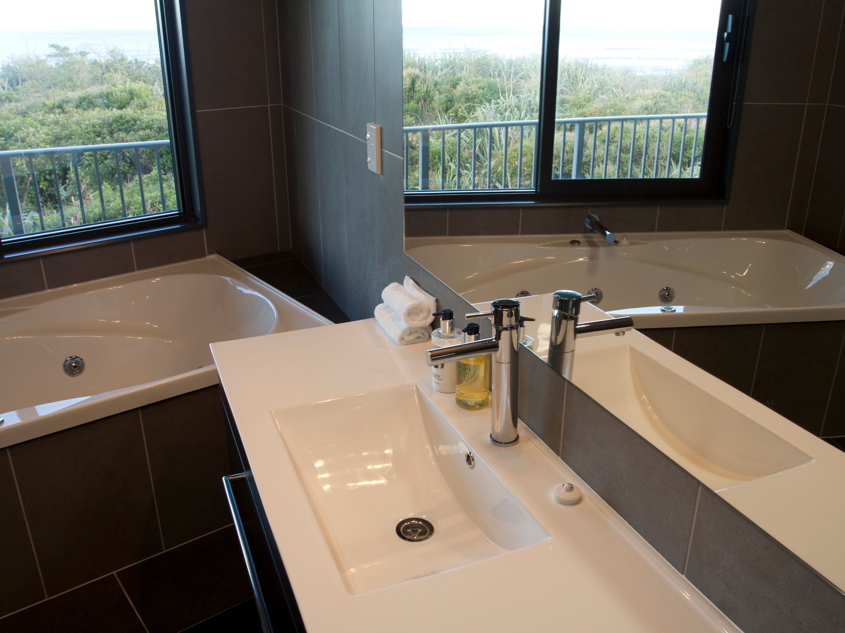 A bathroom with two sinks, a large bathtub, and a window with a view of greenery.