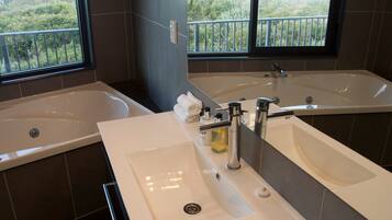 A bathroom with two sinks, a large bathtub, and a window with a view of greenery.