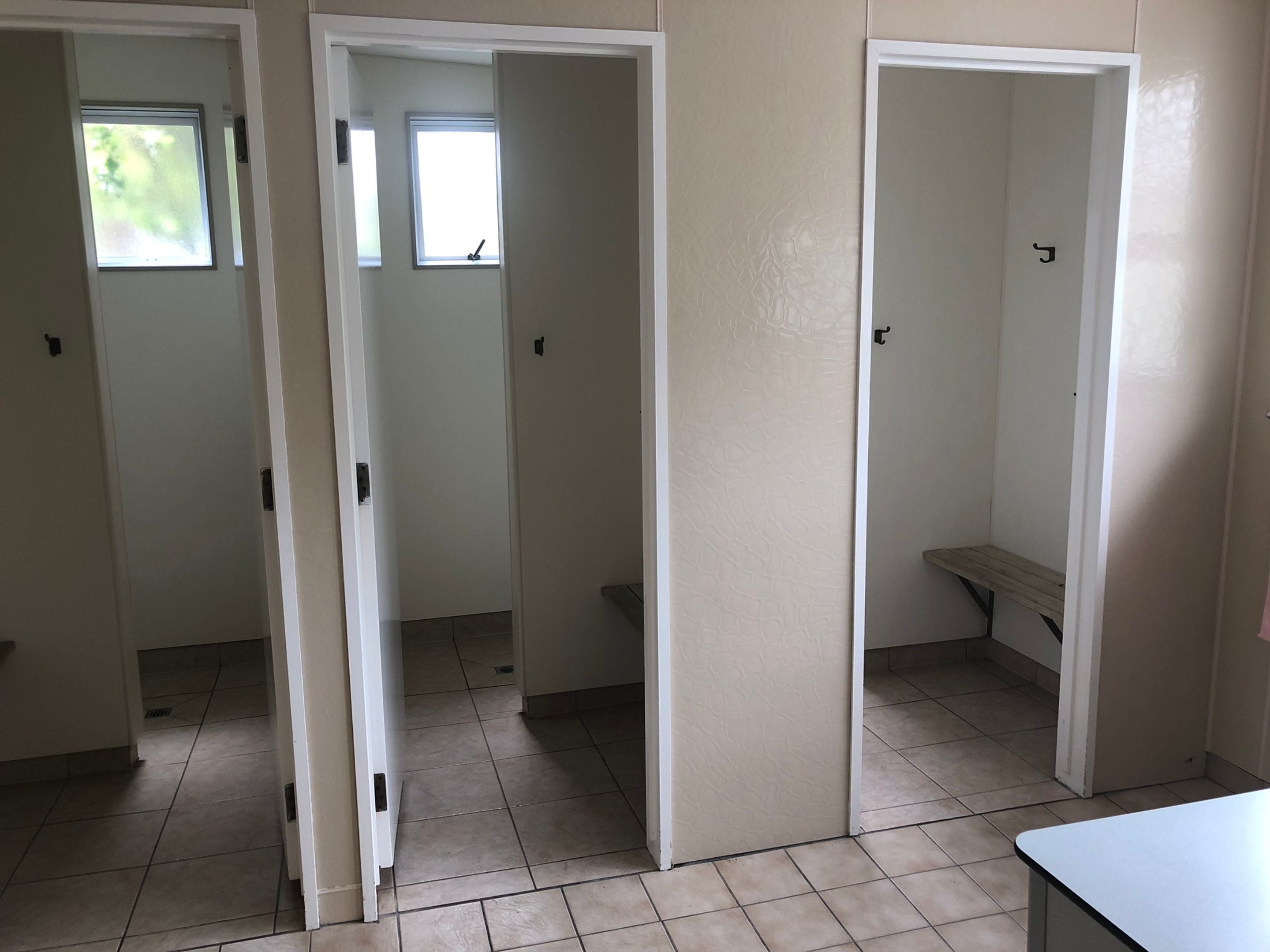 A hallway with three doors, each leading to a different room. The hallway has tiled flooring and a white wall.