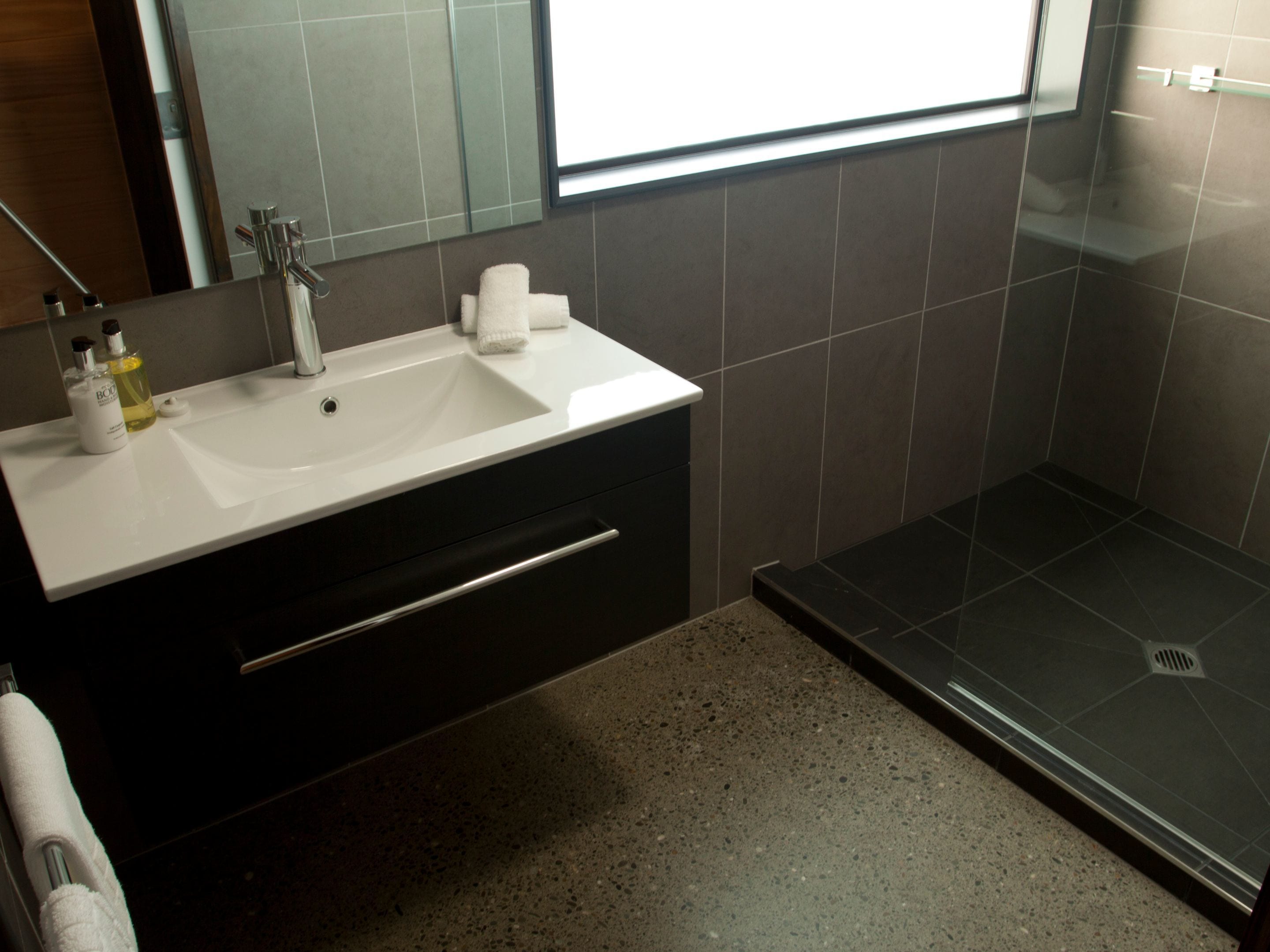 A modern bathroom with a white sink, dark cabinetry, and a glass shower enclosure.