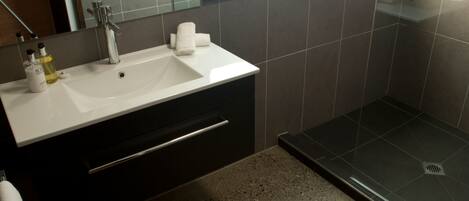 A modern bathroom with a white sink, dark cabinetry, and a glass shower enclosure.