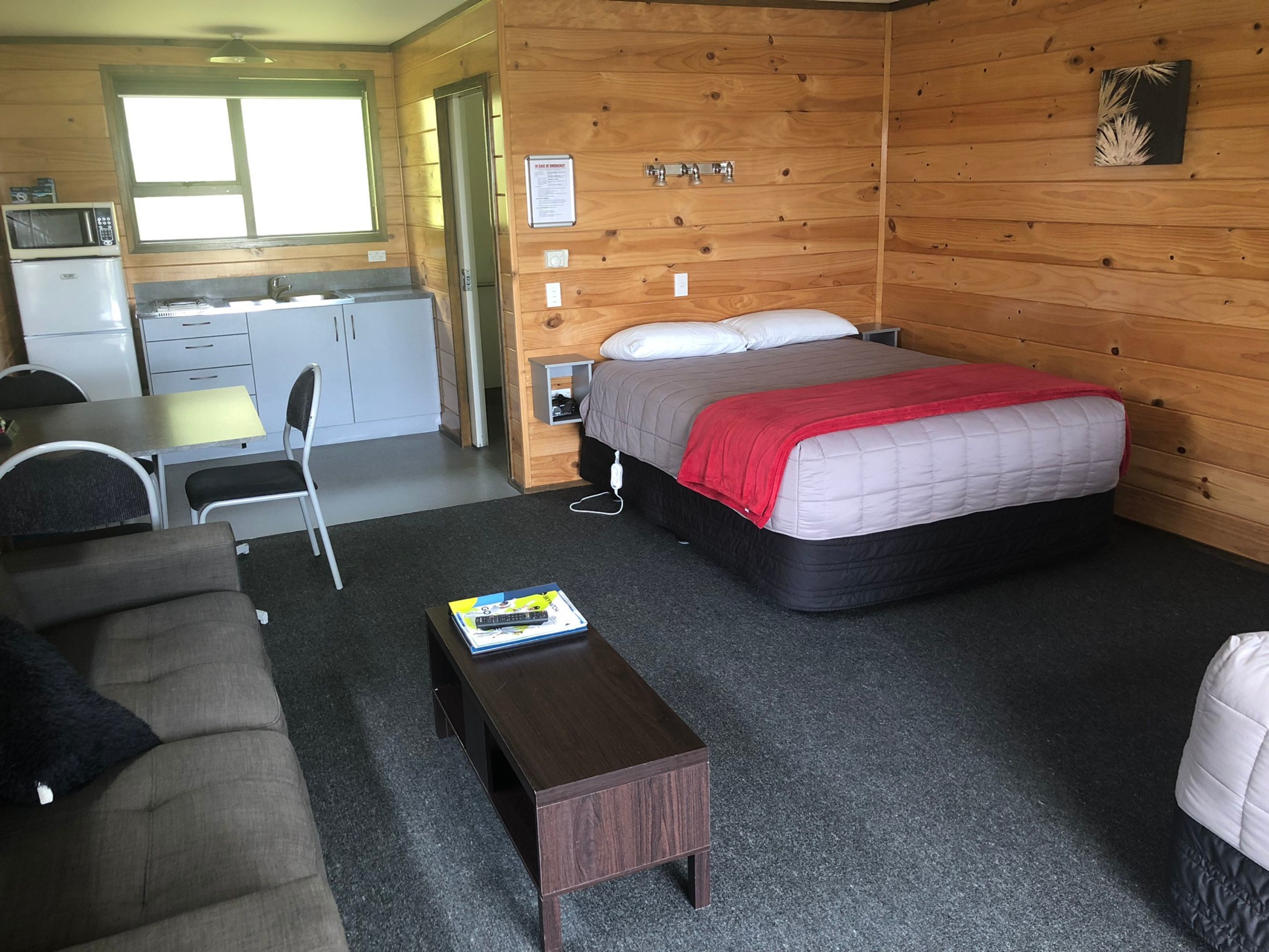 Habitación pequeña con cama, un escritorio, una silla, un microondas y un refrigerador.