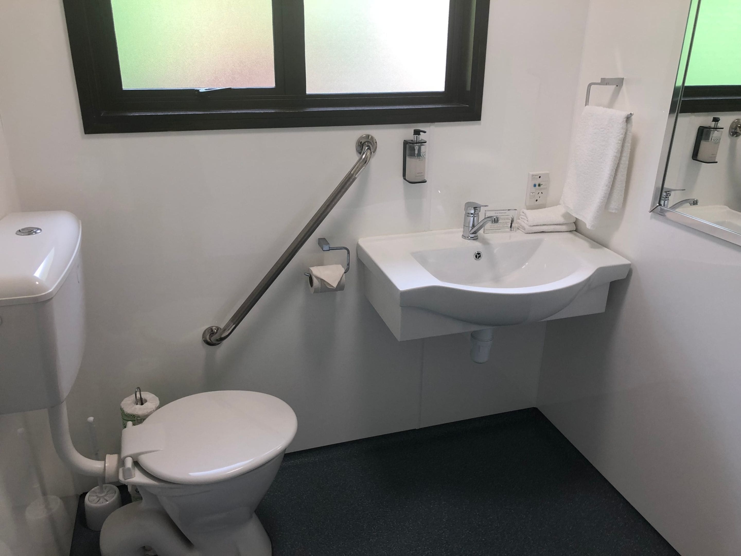 Un baño con inodoro, lavabo, barandilla y ventana.