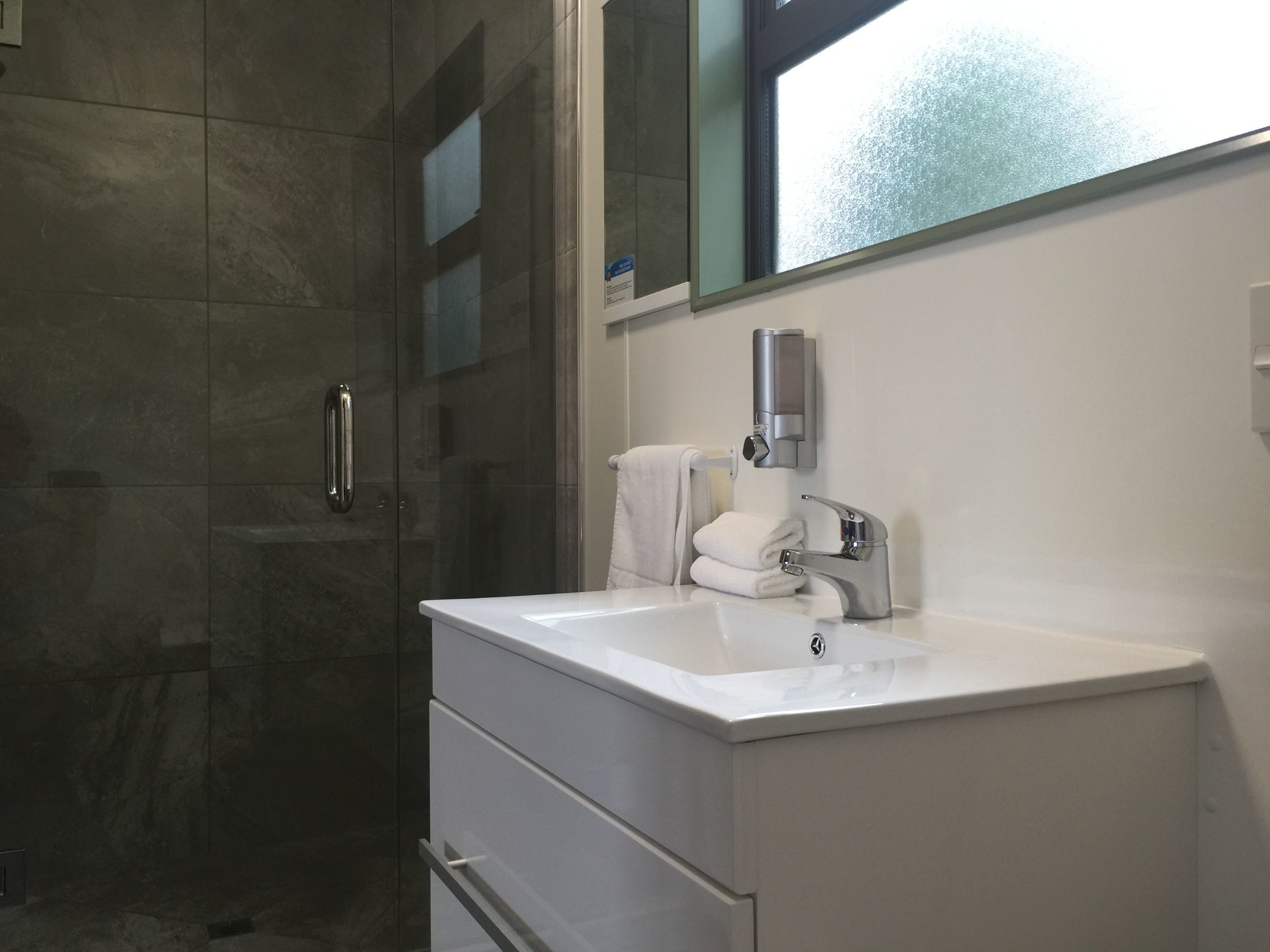 Ein modernes Badezimmer mit einer Duschkabine aus Glas, einem weißen Waschbecken mit Silberarmatur und einem Handtuchhalter.